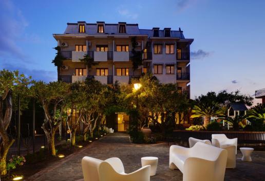 Hotel elegante al tramonto, con giardino illuminato e area relax all’aperto.