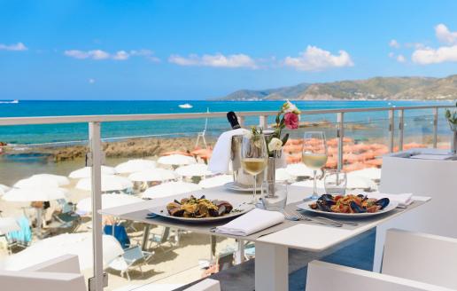 Terrazza sul mare con vista panoramica, tavolo elegante apparecchiato e piatti di pesce.