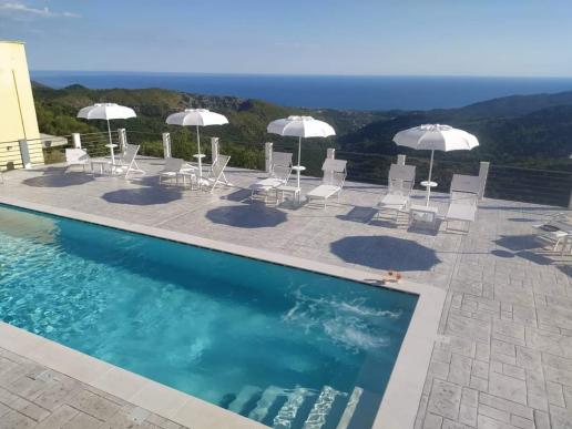 Panorama-Infinity-Pool mit türkisfarbenem Wasser, umgeben von weißen Sonnenliegen und Sonnenschirmen auf einer Steinterrasse.