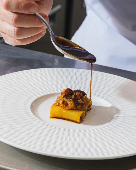 Chef versa una salsa scura su un piatto di pasta ripiena impiattato su un elegante piatto bianco.