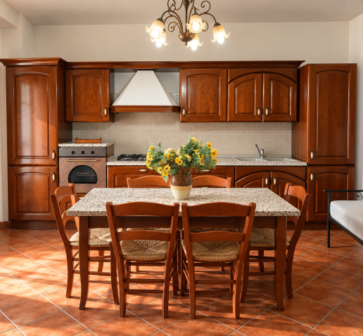 Rustic dark wood kitchen with large dining table, wooden chairs, tiled top and yellow flowers in the center.