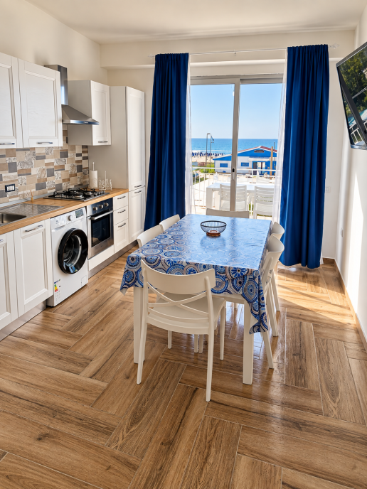 Modern sea view kitchen with dining table and blue curtains.