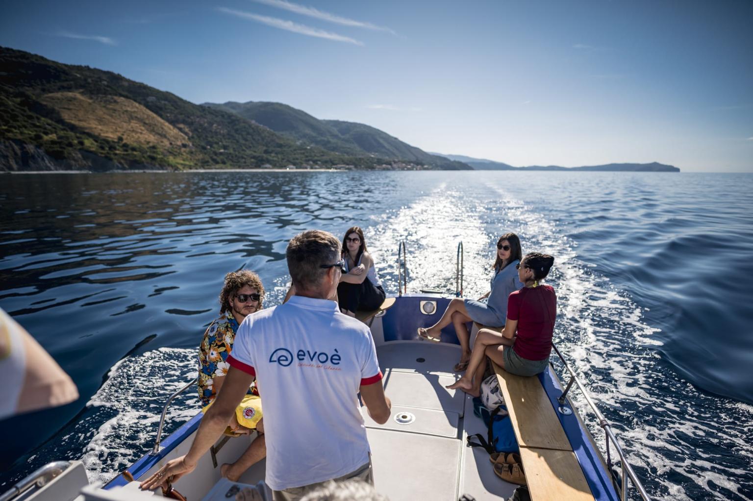 Gita in barca lungo la costa panoramica, con turisti a bordo e mare cristallino illuminato dal sole.