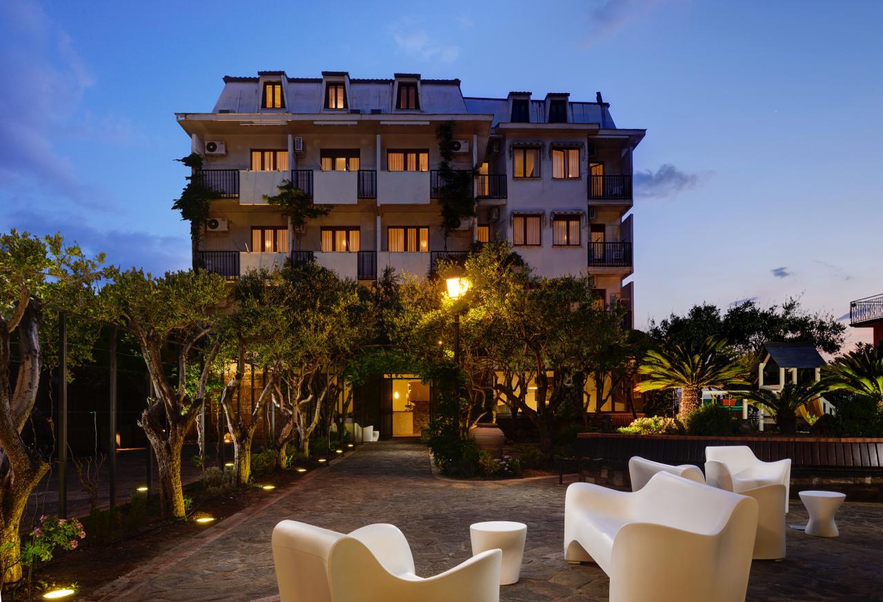 Elegant hotel at sunset, with illuminated garden and outdoor relaxation area.