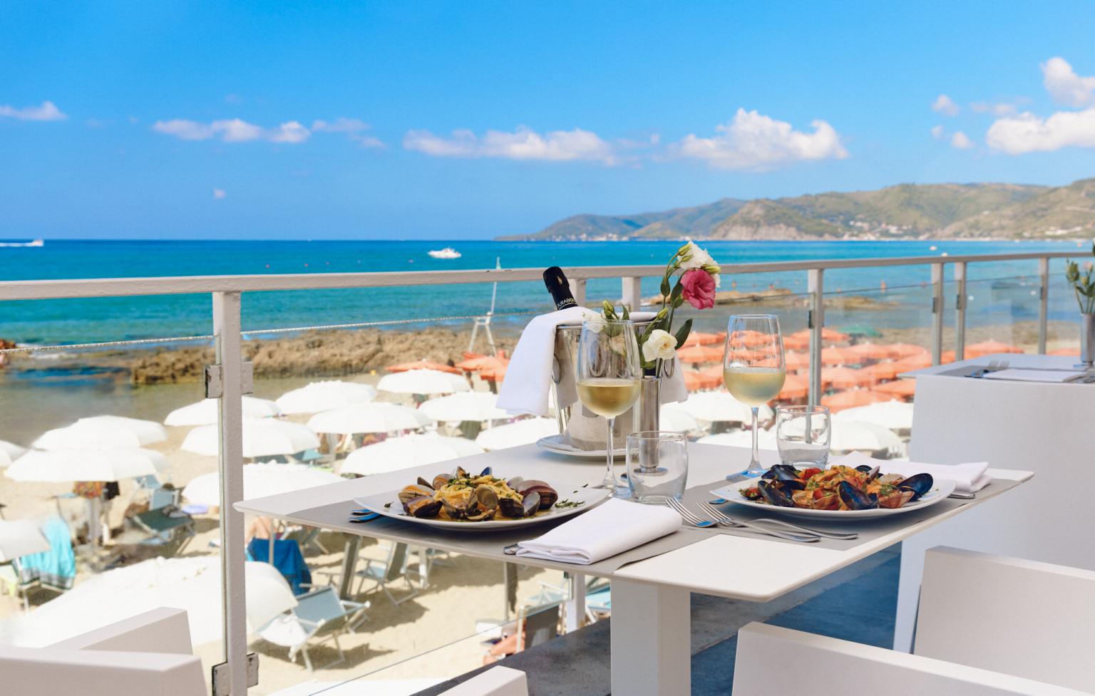 Terrace overlooking the sea with panoramic views, elegantly set table and fish dishes.