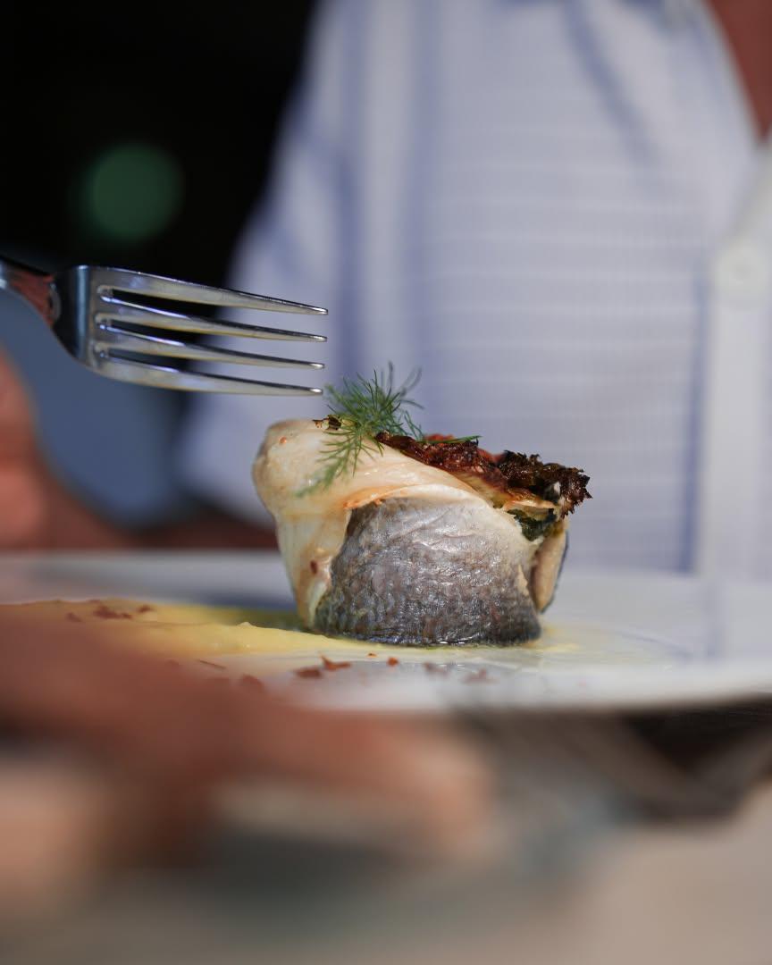 Filetto di pesce al forno impiattato con salsa cremosa, erbe aromatiche e decorazione gourmet.