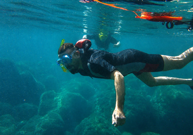 Person practicing snorkeling in crystal clear water, with mask and snorkel.