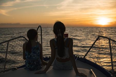 Due ragazze in barca ammirano il tramonto sul mare, immerse nella luce dorata del sole all’orizzonte.