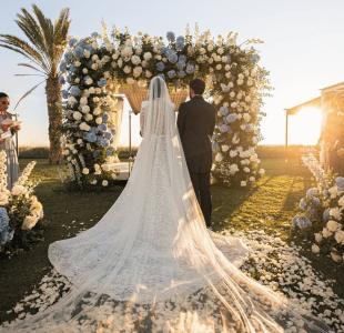Mariage en plein air au coucher du soleil avec les mariés sous une arche fleurie blanche et bleue.