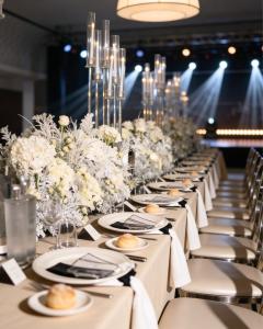 Élégante mise en scène pour un événement, avec une grande table impériale, des fleurs blanches, des candélabres en verre et des assises raffinées.