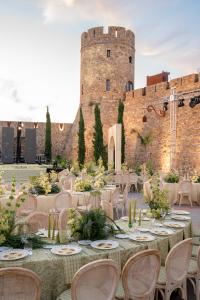 Allestimento elegante per matrimonio in una corte storica con tavoli decorati, sedie provenzali e composizioni floreali dai toni naturali, ai piedi di un castello in pietra.