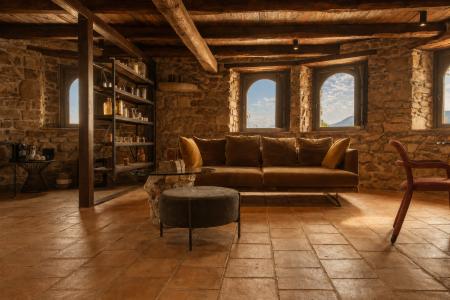 Salon rustique avec murs en pierre apparente, poutres en bois, sol en terre cuite et canapé en cuir marron, baigné par la lumière naturelle des fenêtres panoramiques.