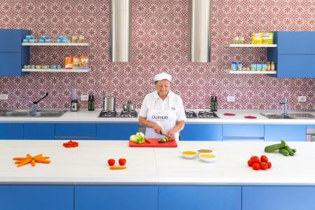 Chef preparing fresh vegetables in a professional baby food preparation room with blue furnishings and decorated walls.