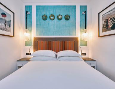 Chambre élégante avec lit double, tête de lit décorative à rayures orange et bleues, mur turquoise, appliques lumineuses et détails de design raffinés.