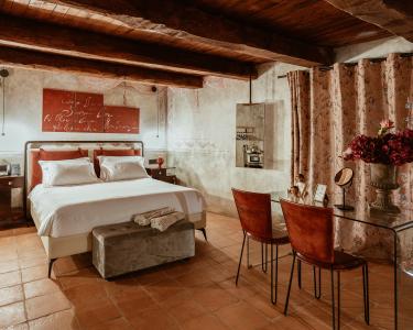 Chambre à coucher au style rustique élégant, avec poutres apparentes en bois, sol en terre cuite, lit double avec linge de lit blanc et mobilier aux tons chaleureux.