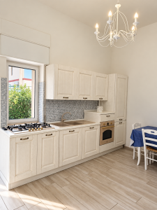 Bright and modern kitchen with white cabinets, cooktop, oven, sink and dining table.