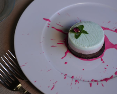 Dolce al pistacchio con base al cioccolato, decorato con menta e petali di fiore.