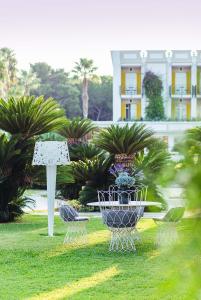 Jardin élégant avec une table et des chaises blanches en fer forgé, des palmiers et une végétation luxuriante.