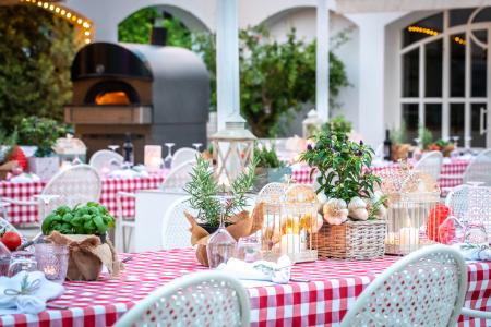 Tables set with checkered tablecloths, floral decorations, and a wood-fired oven in an elegant outdoor restaurant.