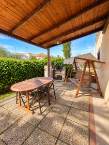 Large outdoor patio furnished with a wooden table and chairs, covered swing and built-in barbecue.