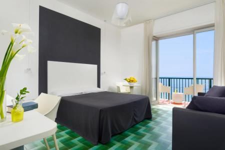 Modern and bright bedroom with a double bed, elegant furnishings, large glass window, and sea view.