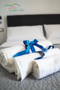 Weiße Handtücher, zu Rollen gefaltet und mit einem blauen Band gebunden, auf einem Bett in der Unterkunft La Valle del Ciglioto.