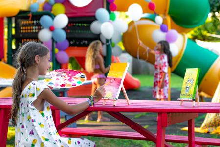 Little girl painting on a canvas during a children's party decorated with colorful balloons and inflatable play equipment.