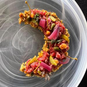 Tartare di manzo gourmet con cipolla rossa, cetriolini, capperi e crumble croccante.