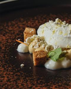Gourmet dessert featuring vanilla ice cream, caramel cream, crunchy crumble and fresh sorrel leaves, served on a dark plate.