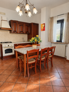 Rustic dark wood kitchen with large dining table, wooden chairs, tiled top and yellow flowers in the center.