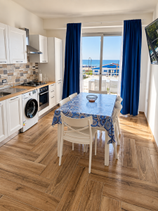 Bright and modern kitchen with dining table, blue curtains and sea view.