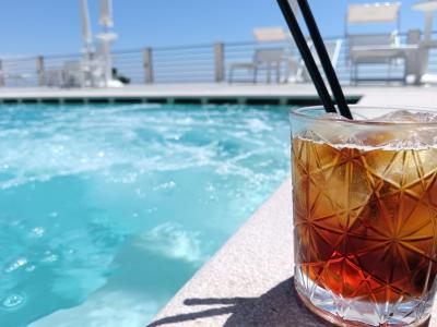 Bernsteinfarbener Cocktail mit Eis, serviert in einem eleganten, geschliffenen Glas am Pool, mit türkisfarbenem Wasser und Sonnenliegen im Hintergrund.