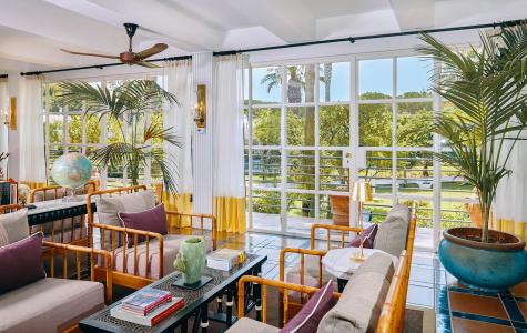 Véranda lumineuse de style tropical, avec du mobilier en bambou, des plantes ornementales et de grandes baies vitrées donnant sur le jardin.