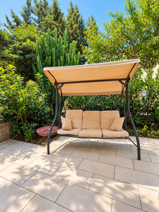 Garden swing with a metal frame and beige cushions, surrounded by greenery.