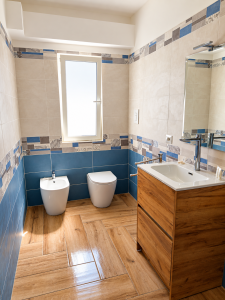 Modern bathroom with beige and blue tiles, wooden vanity unit, white sanitary fixtures and wood-effect flooring.