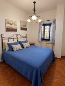 Rustic-style double bedroom with a wrought-iron bed, blue bed linen, bedside tables and a window with curtains.