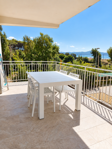Panoramic sea-view terrace with white table and chairs, surrounded by greenery.